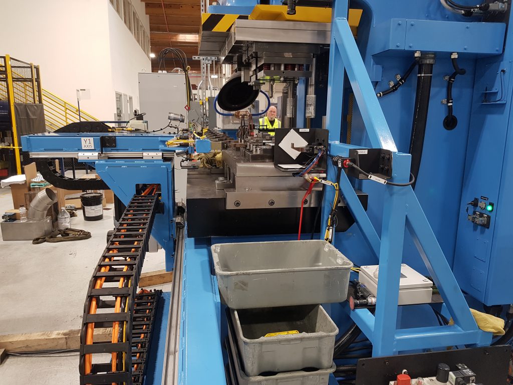 An image of a blue, forging machine with a custom Linear Automation transfer system.